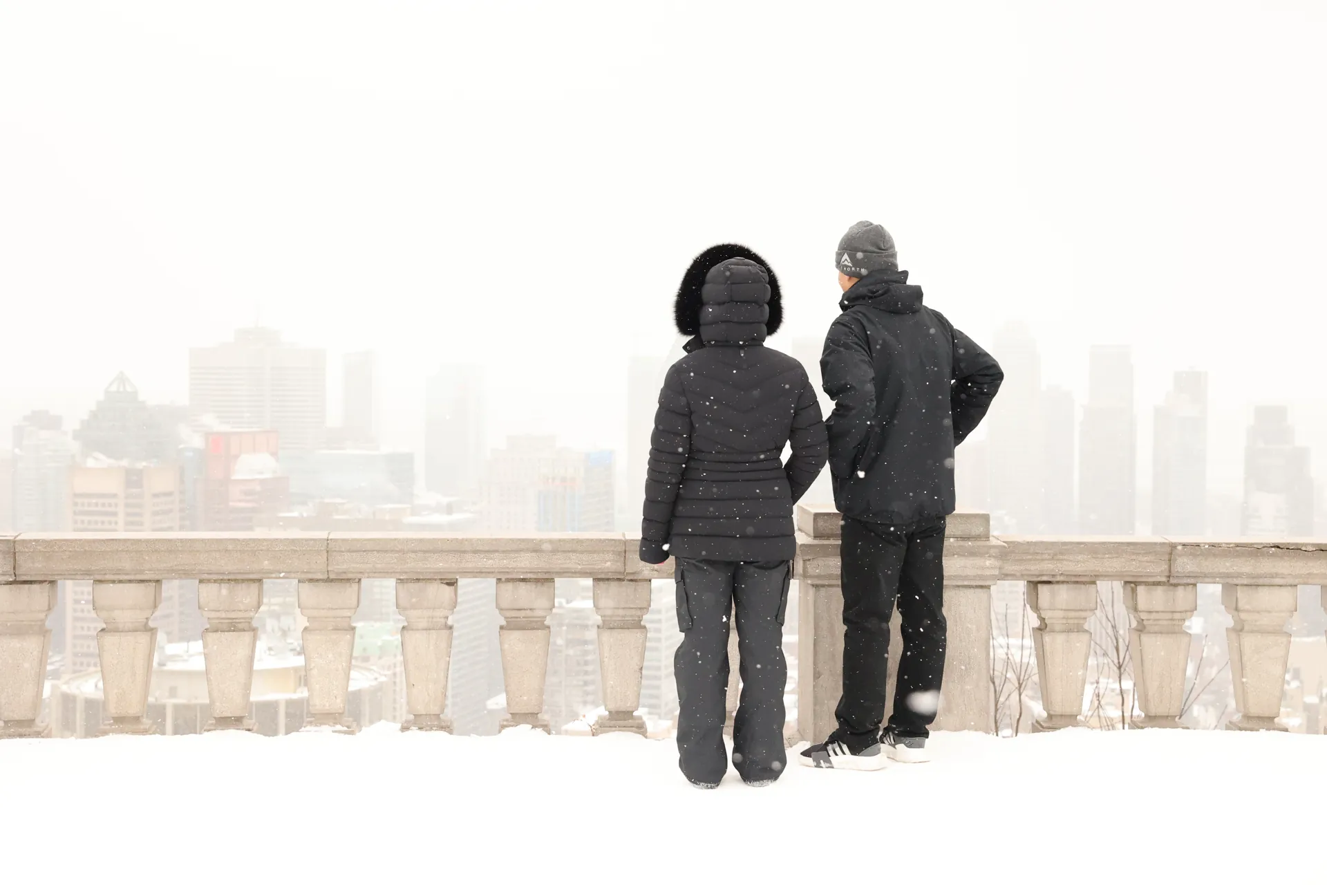Deux silhouettes emmitouflées devant une balustrade et la ville dans la brume