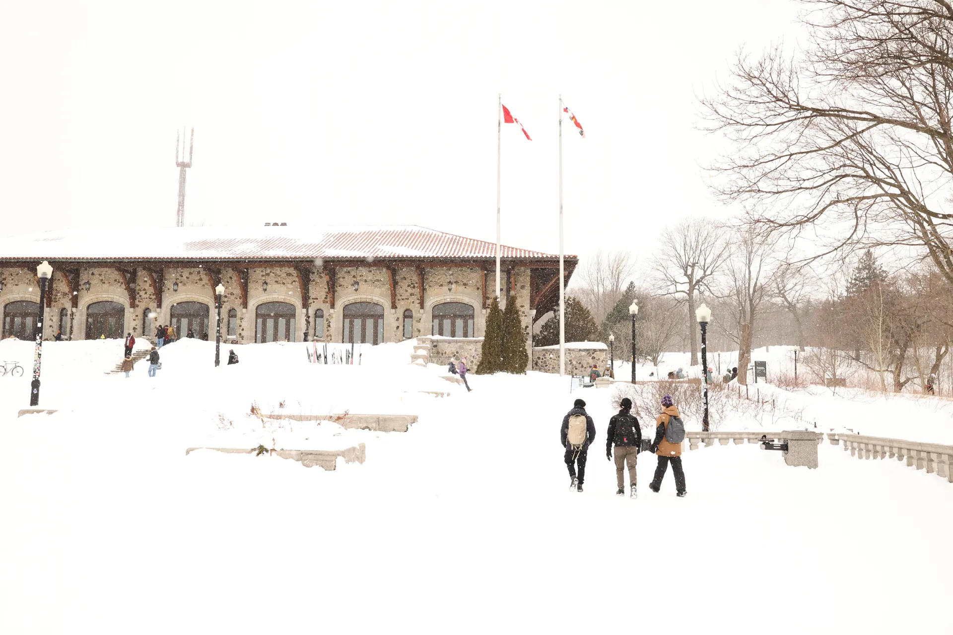 Bâtiment au bord d’une esplanade enneigée avec promeneurs et drapeaux