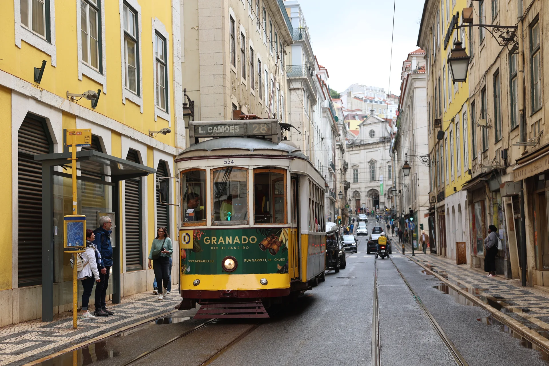 Un tramway jaune dans une rue de Lisbonne, entre rails et façades.