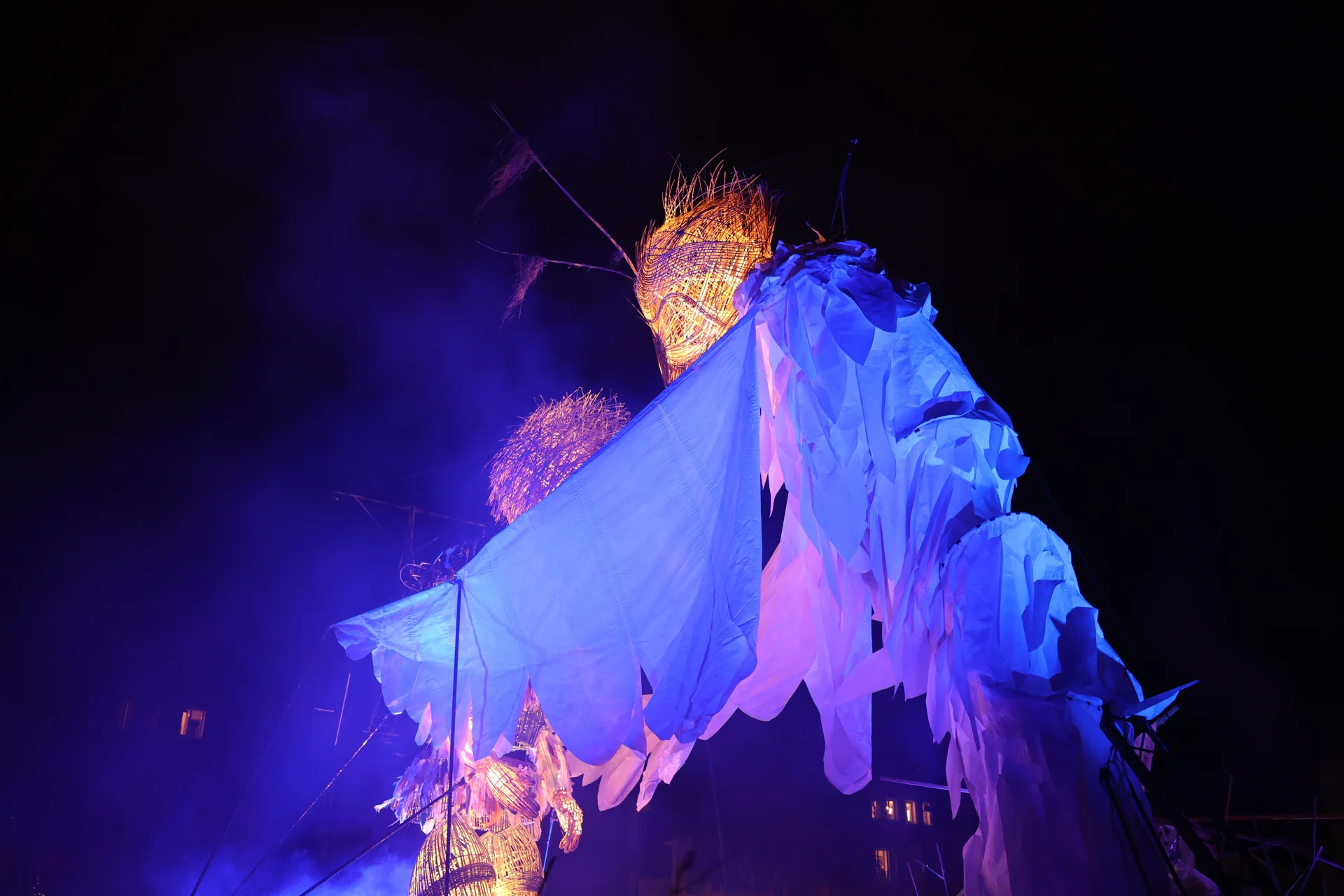 Un personnage-oiseau aux ailes bleues éclairées pendant le spectacle.