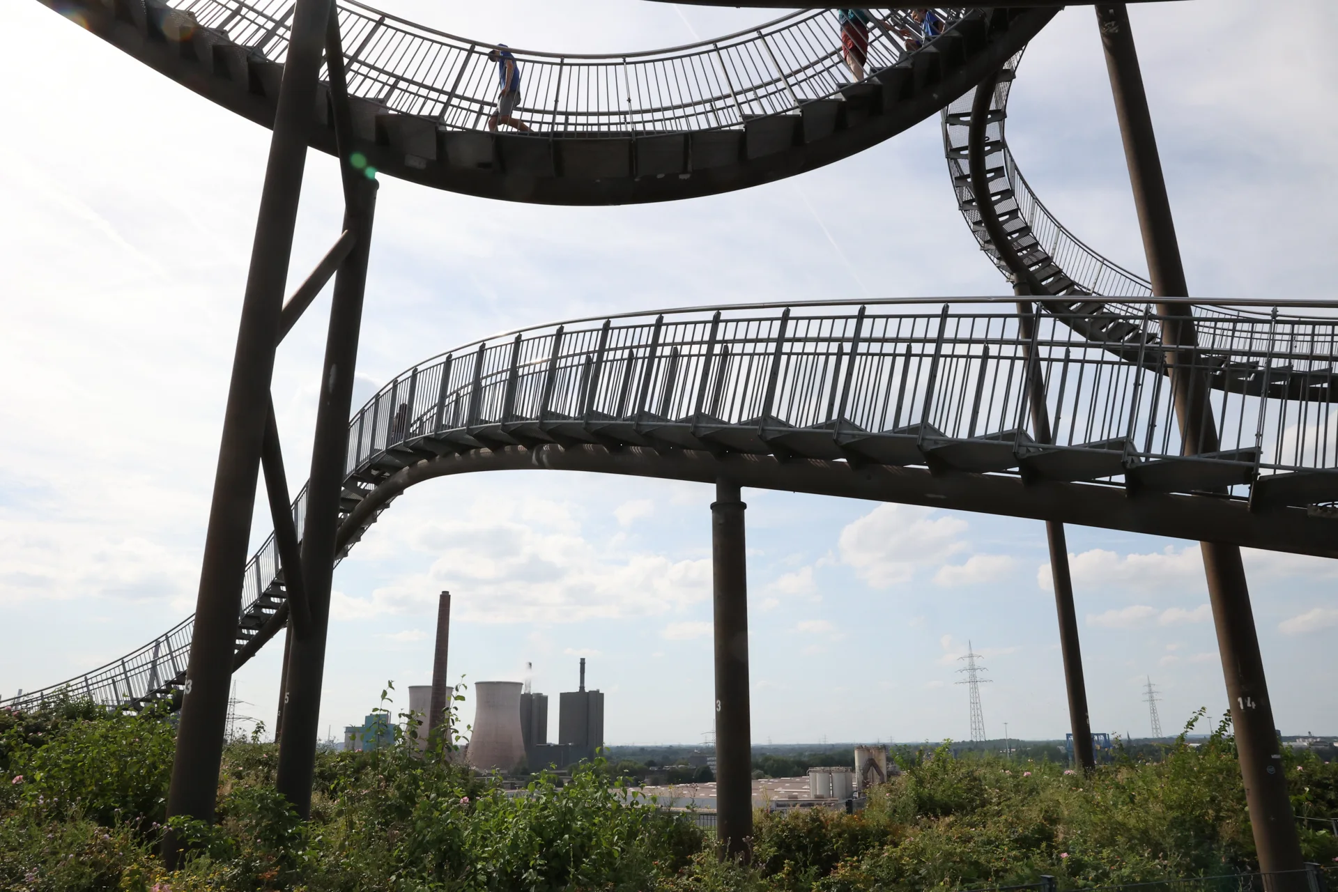 Les cheminées et bâtiments industriels apparaissent entre les supports de la sculpture.